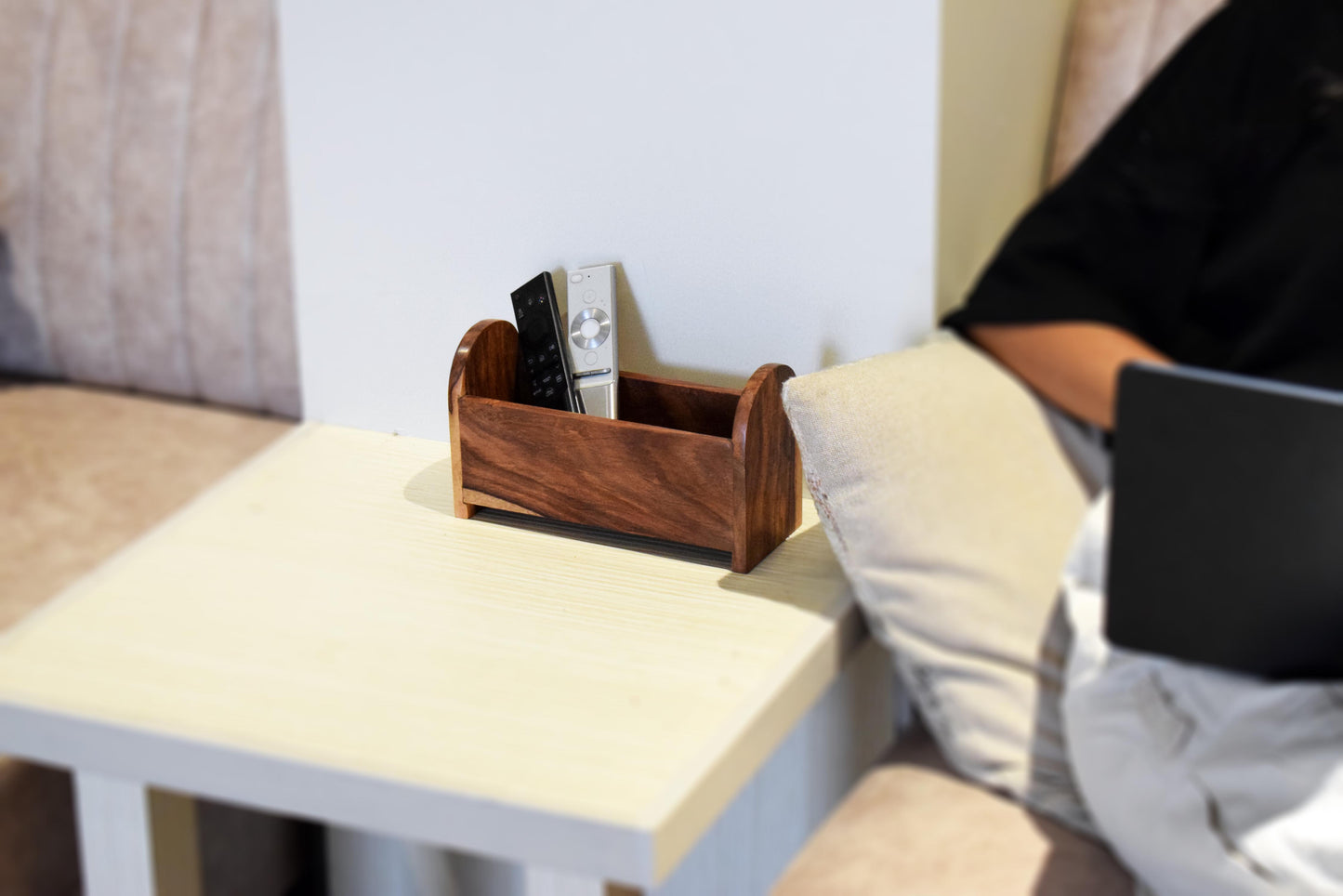 Person sitting on a couch using a laptop with a wooden remote holder on a side table.