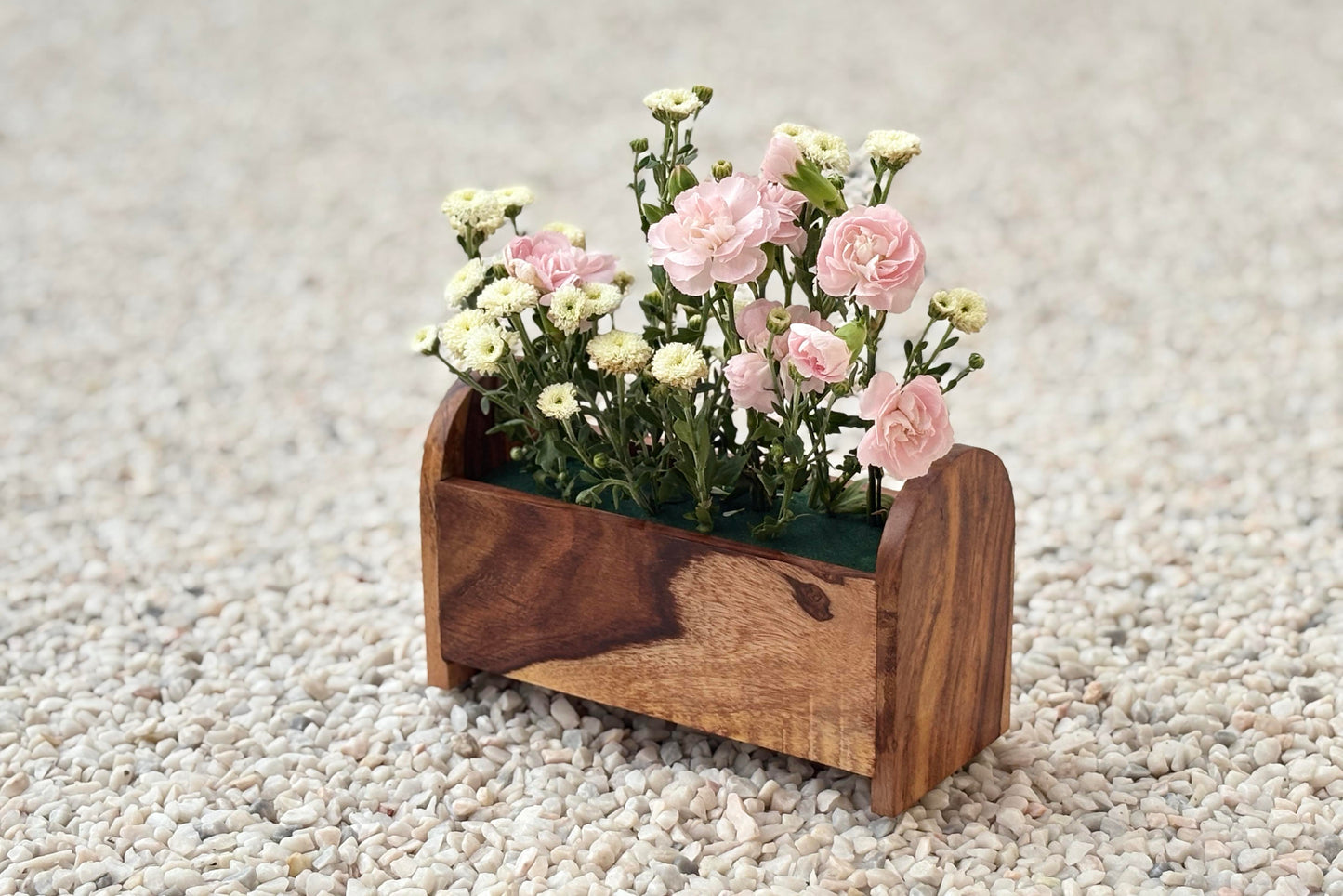 Wooden planter with flowers on a pebbled surface