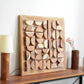 Wooden wall art piece on a shelf with a lamp and vase in the background