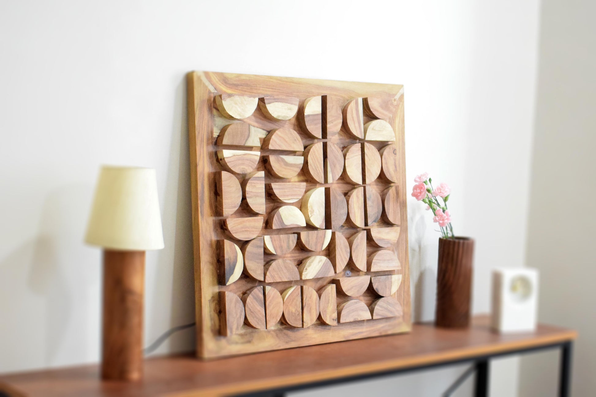 Wooden wall art piece on a shelf with a lamp and vase in the background