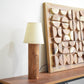 Wooden lamp, decorative wall art, and vase on a shelf against a white wall