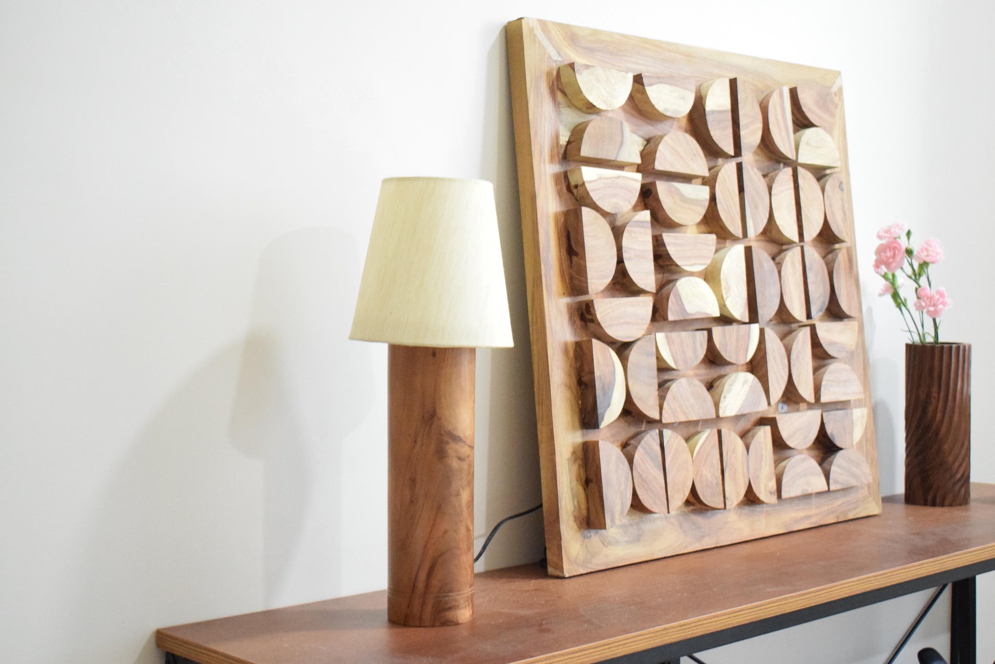 Wooden lamp, decorative wall art, and vase on a shelf against a white wall