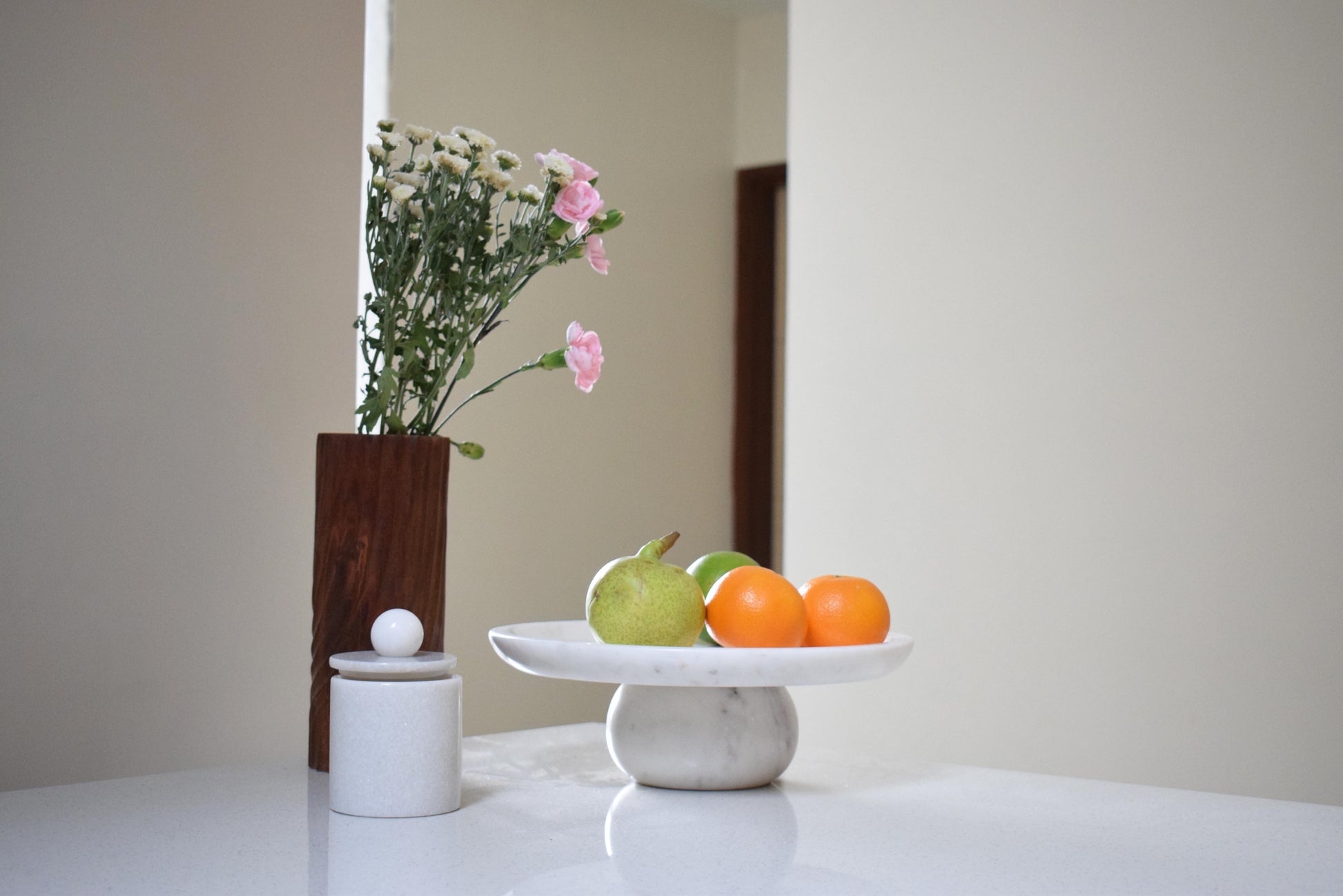 Fruits on a white fruit stand with a vase of flowers in the background