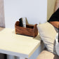 Person sitting on a couch using a laptop with a wooden remote holder on a side table.