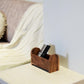 Wooden remote control holder on a shelf with a blurred sofa in the background