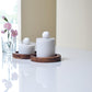 Two white cylindrical marble food jars with wooden tray, with pink flowers in the background.